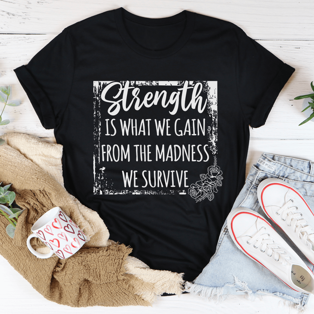 Black Heather Strength Is What We Gain From The Madness We Survive T-Shirt motivational graphic t-shirt on a casual flatlay.