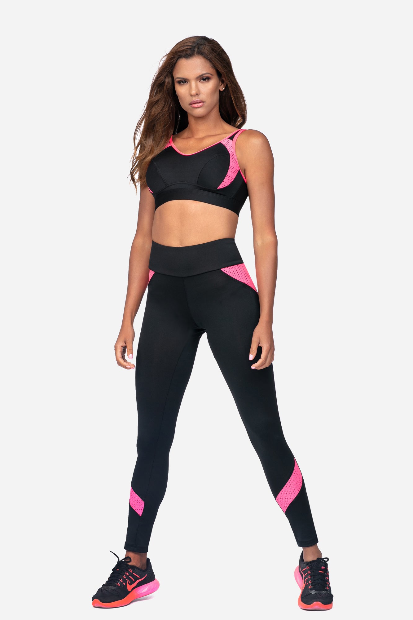 Women's black pink sports bra for training modeled with matching leggings and athletic shoes.
