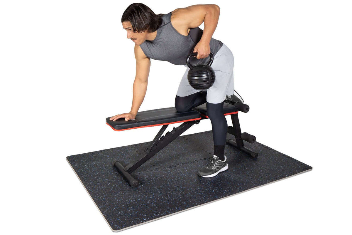 Man performing exercises on a rubber top exercise mat with a dumbbell for strength training.