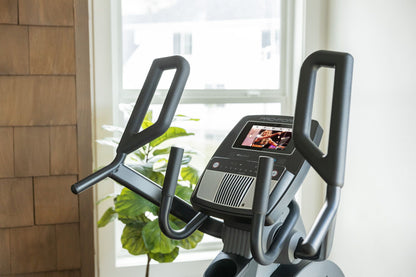 Fitness Essentials Trainer H7 iFit-enabled elliptical with 7-inch touchscreen and built-in fan, showing the sleek console and elliptical frame.