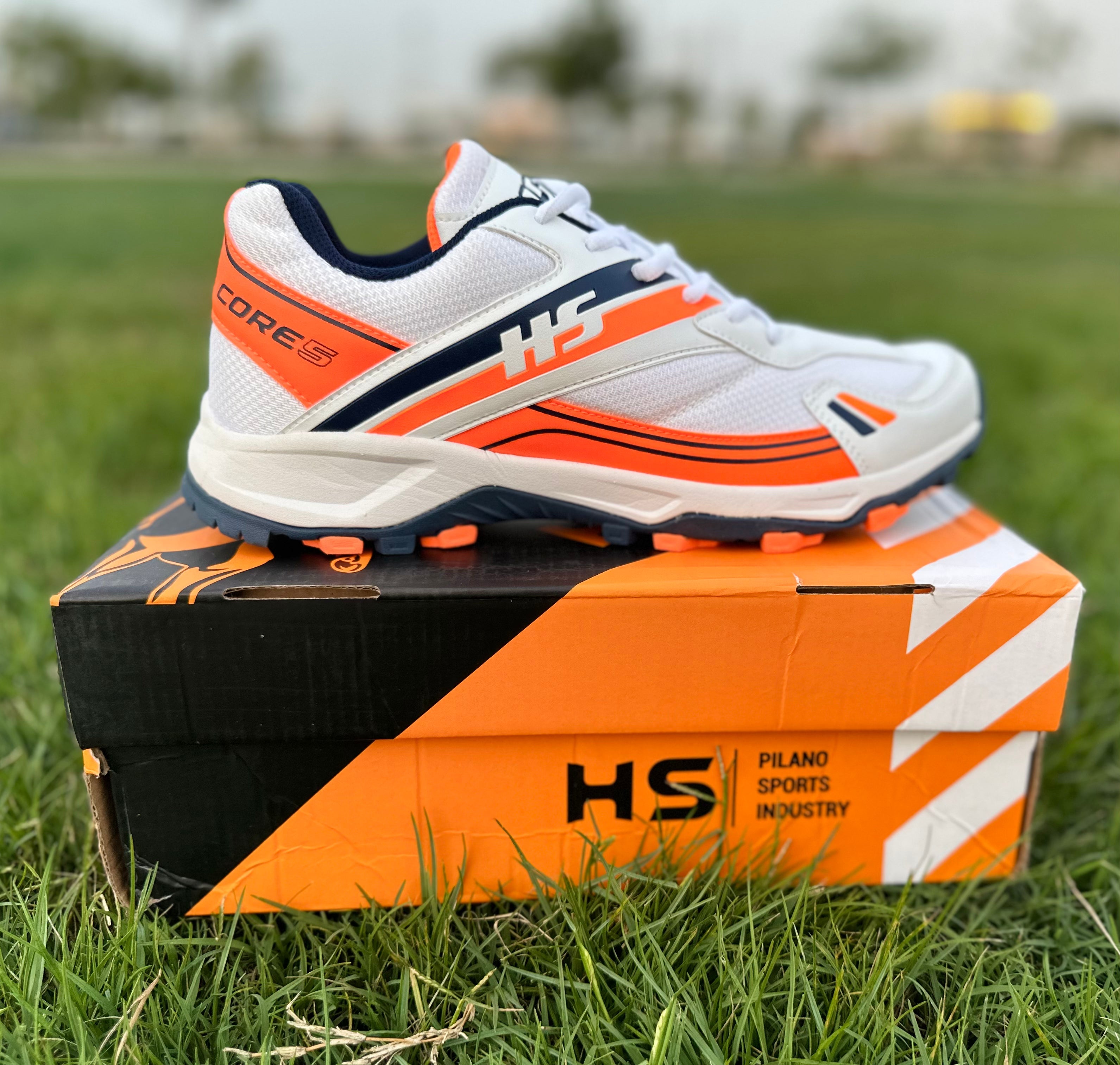HS Core-5 lightweight cricket shoes for performance in red, size EUR 42, showcasing breathability and traction on a grassy field.