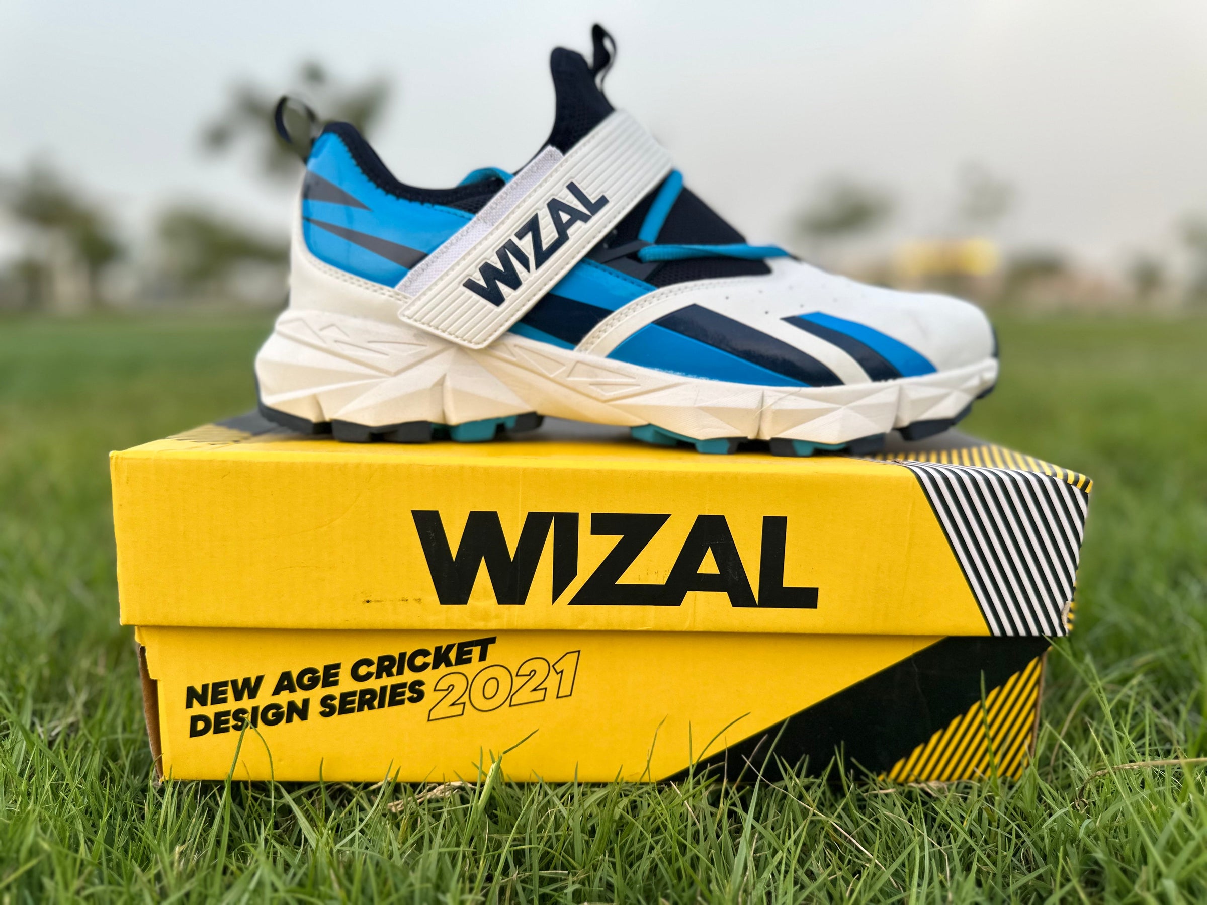 Wizal cricket shoes for enhanced stability displayed on a yellow box, size EUR 44, featuring a blue color scheme and rubber grip.