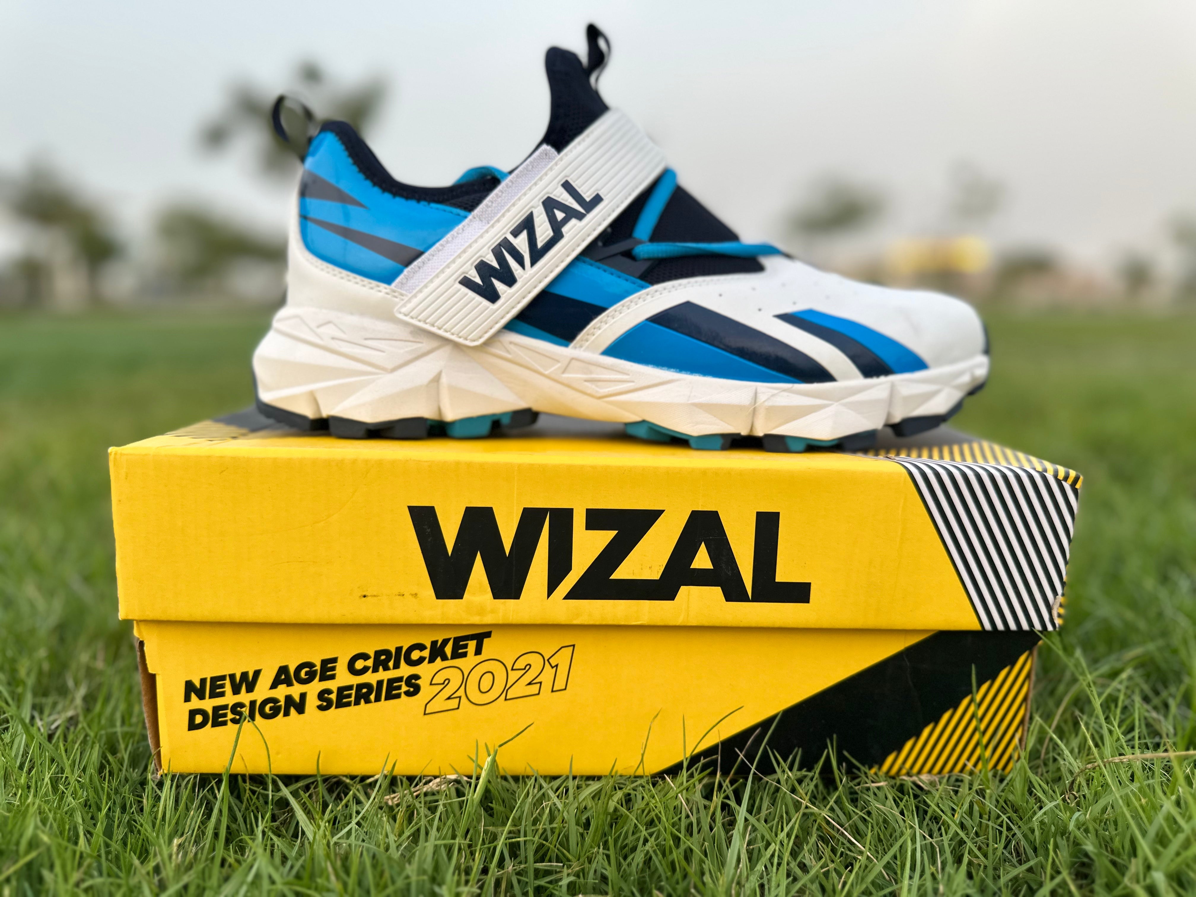 Wizal cricket shoes for enhanced stability displayed on a yellow box, size EUR 44, featuring a blue color scheme and rubber grip.