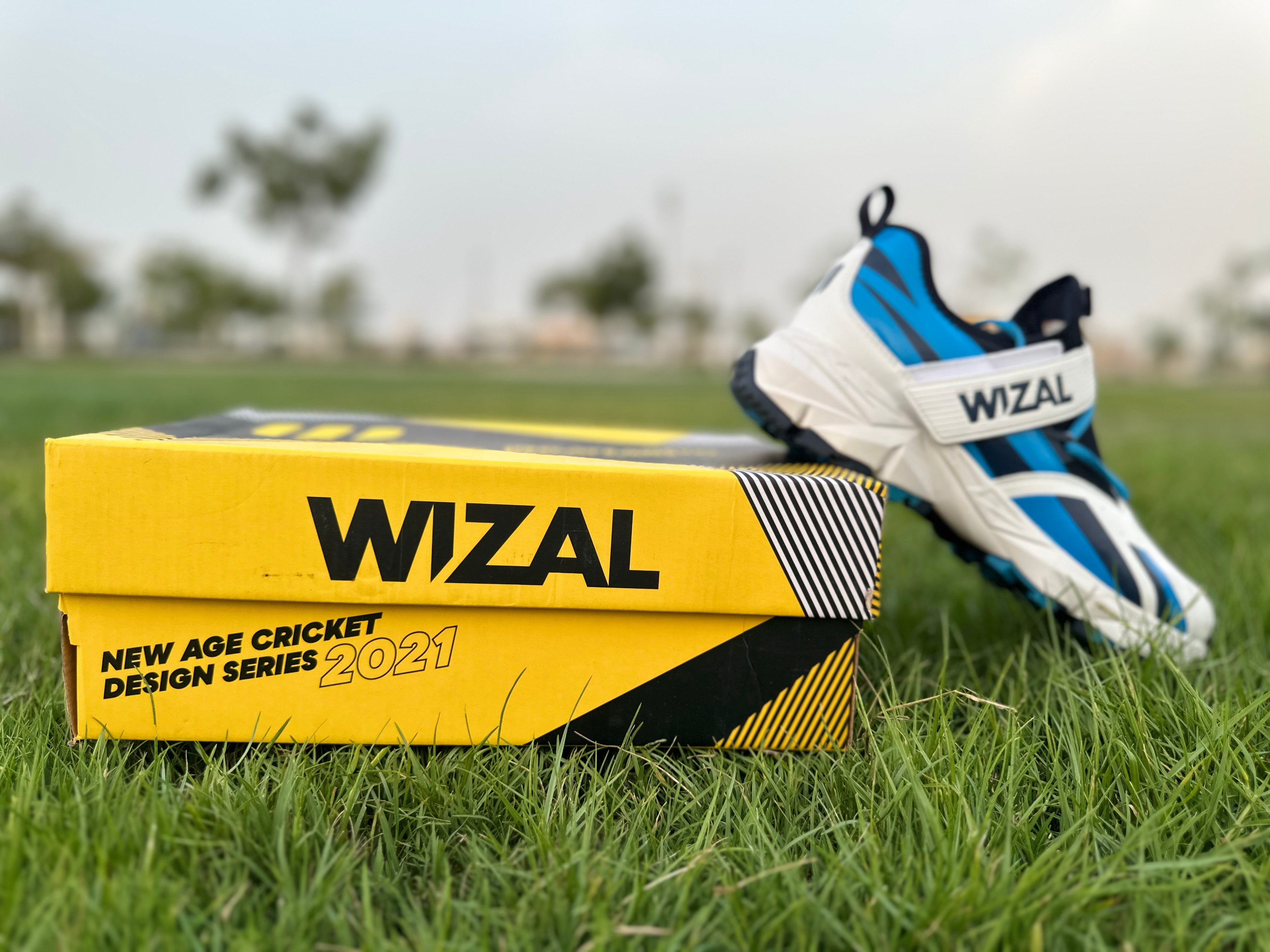 Wizal cricket shoes for enhanced stability, EUR 42 size, blue color, alongside yellow packaging on grass.