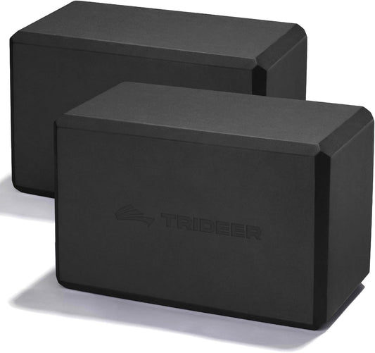 Two black yoga blocks made of soft non-slip foam with beveled edges, used for alignment and stretching in yoga and Pilates.